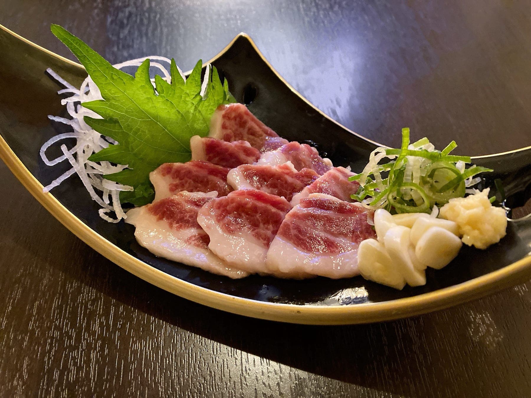 サシの入った霜降りの馬刺し。黒い器に大葉と薬味を添えて