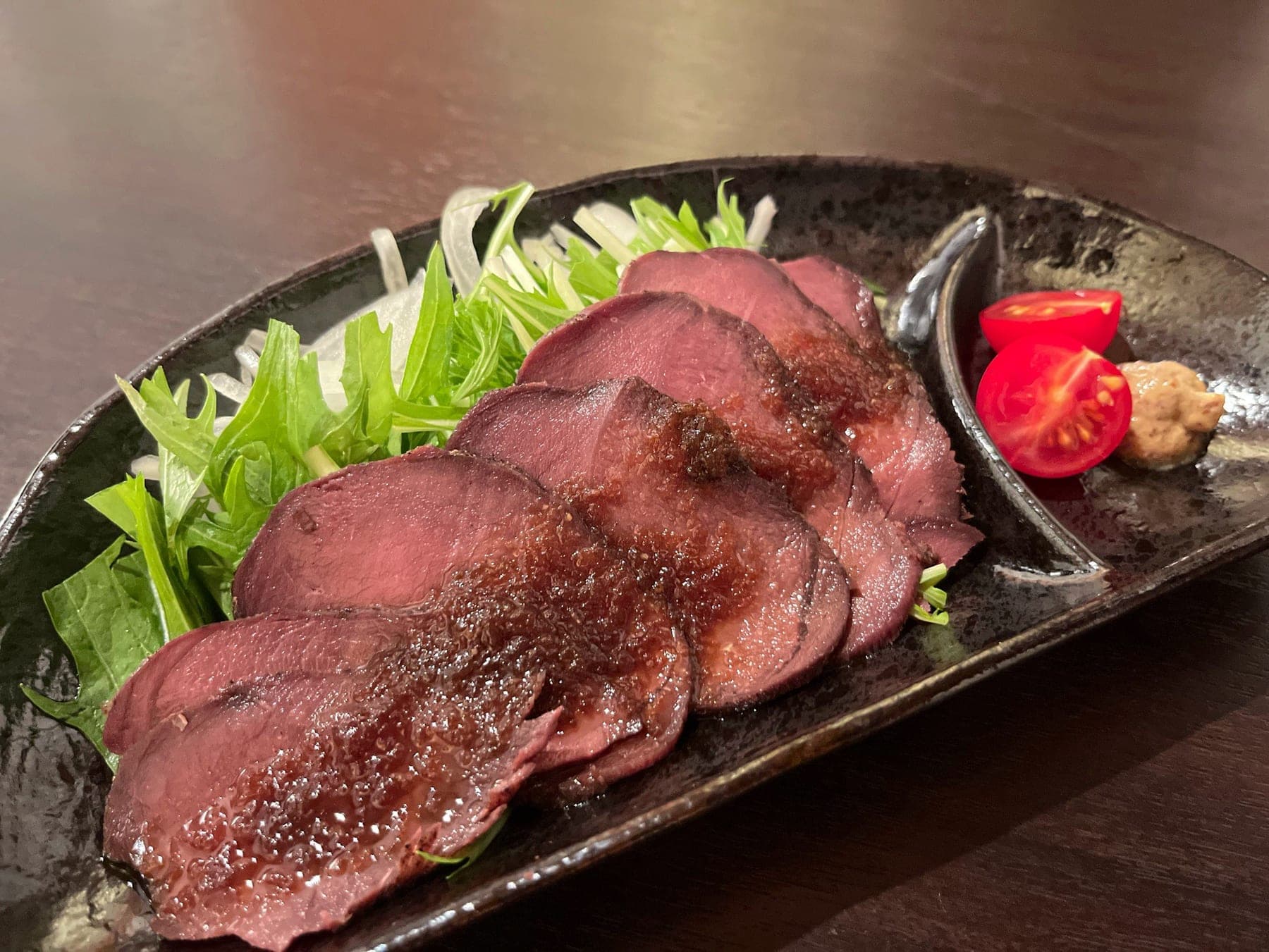 ソースをかけた肉の一品料理。水菜とミニトマトを添えて
