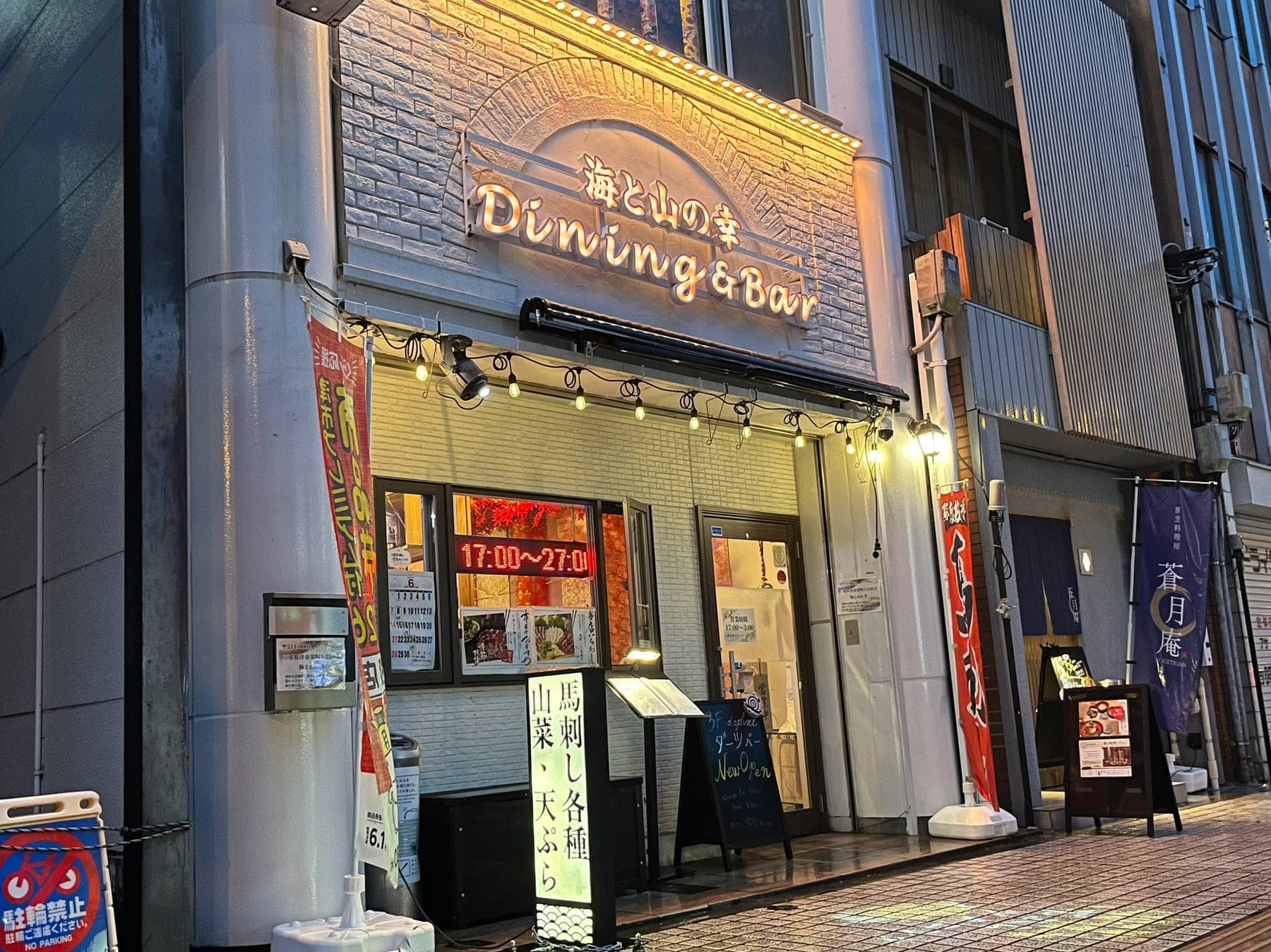 営業時間の電光掲示と「馬刺し各種・山菜・天ぷら」の行灯が並ぶ店先